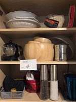 Overview of shelves with grinders, wooden bowls, pie plate, baking dishes, teapot, baskets and other items