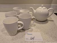 Teapot with lid and five mugs displayed together on countertop