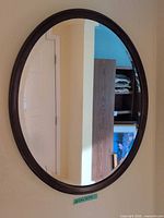 Front view of oval dark brown wood wall mirror mounted on wall
