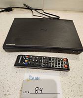 Top view of Samsung Blu-ray player with remote control and attached power cord visible