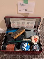 Open red tin showing brushes, polish tins, cloths