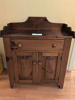 Front view of solid wood cabinet showing drawer, two doors, raised backsplash