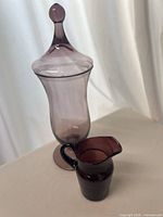 Tall amethyst footed vase with lid beside small ribbed pitcher