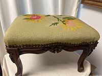 Three-quarter view of stool showing needlepoint top and carved frame