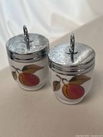Front view of both egg coddlers showing fruit motif and lids