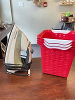 Steam iron standing upright next to stacked red plastic baskets