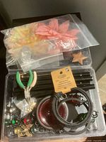 Overview of clear storage box with pliers, cords, charms, beads, star pendant, bells, and bag of flowers