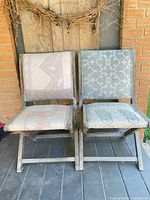 Front view of both folding chairs showing upholstery patterns and weathered wood