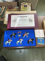 Closed presentation box with illustrated lid and interior showing blue felt tray with figures and accessories