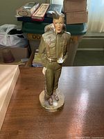 Front view of plaster soldier figurine standing on round base, shows full height and facial detail
