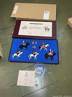 Presentation box open showing five mounted figures, accessories, certificate, booklet