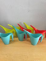 Seven plastic watering cans assorted colors on table