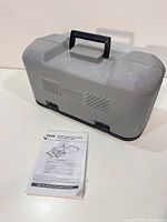 Gray Ryobi hard case closed beside manual