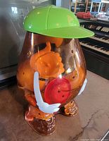 Front view of Giant Mr. Potato Head container showing green cap, white arms, amber body filled with parts
