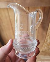 Front view of clear glass creamer showing etched text and beaded band