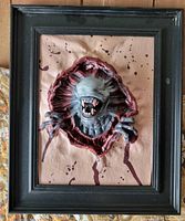 Front view of framed 3D rubber alien chest-burster decor showing creature, faux flesh backdrop, and frame