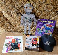 Group shot of all five items on table: cardboard robot cut-out, Japanese book, Balloon Robot kit box, Make-A-Mask kit, navy Robot cap