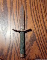 Full view dagger on wood surface showing blade, guard, handle, pommel