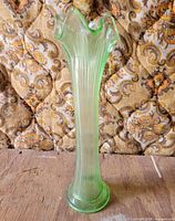 Full view of tall green uranium glass vase standing upright on wood surface with patterned background