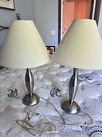 Both brushed nickel table lamps with beige shades on bed