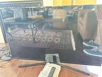 Front view of Samsung 48" TV on stand with remote, manual and cables visible