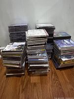 Three tall stacks of assorted CD jewel cases on wooden floor