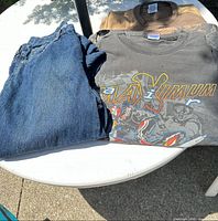 Graphic T-shirt, brown hoodie partially visible, blue jeans folded