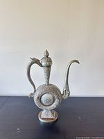 Front view of decorative brass ewer showing circular body, spout, handle, lid and base