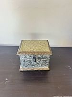 Closed view of ornate metal jewelry box showing embossed lid, latch, patina