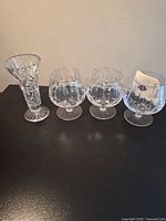 Bud vase and three brandy snifters on black surface