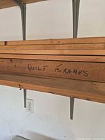 Wooden quilt frame rails stacked on wall shelf, handwritten label visible
