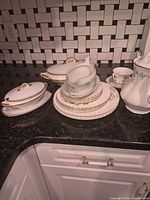 group shot of stacked plates, gravy boat, covered dish, teapot, cup and saucer on countertop