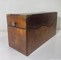 Front angled view showing leather exterior, brass knob, corner protectors and wavy trim