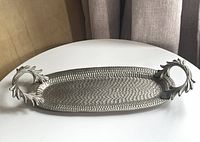Full view of textured metal tray with leaf handles on white surface