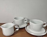 Two porcelain cups on saucers and milk pitcher showing set