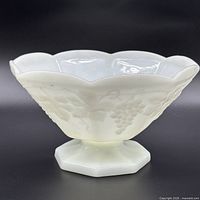Side view of white milk glass pedestal bowl showing grape vine relief and octagonal base