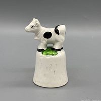 Front view of porcelain bell with cow figure on green base