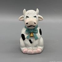 Front view of ceramic cow figurine showing colors, scarf, bell, pink hooves