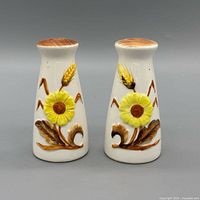 Front view of both ceramic shakers showing floral and wheat relief design
