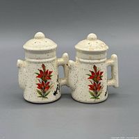 Front view of both cream speckled shakers displaying red floral design and Saskatchewan marking