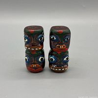 Front view of four stacked tiki shakers showing painted faces