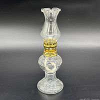 Full view of clear glass oil lamp with brass burner and chimney