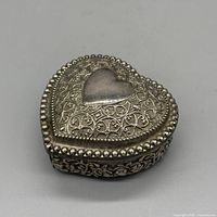 Top view of heart-shaped silver-plated trinket box showing embossed filigree lid and beaded edging