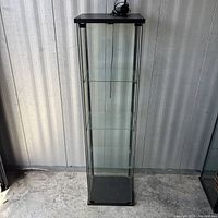 Full front view of tall glass cabinet showing three shelves and top light cord