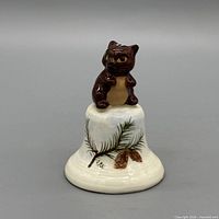 Front view of porcelain bell showing cat figurine and pinecone motif