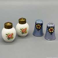 Group shot of all four shakers: two white rounded with brass tops and floral decals, two blue conical with painted flowers