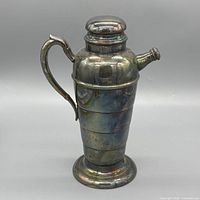 Front view of silver-plated cocktail shaker showing handle, spout, lid and patina