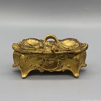 Front view of gilt brass jewelry box showing ornate relief and handle