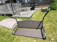 Full view of swing seat with metal frame arms and wicker panels on grass
