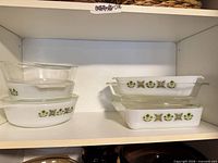 Shelf view showing two round and two rectangular Fire-King Spring Blossom casseroles with lids